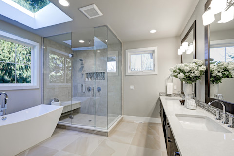 Un bagno spazioso nei toni del grigio con vasca da bagno freestanding ed elegante doccia con box in vetro, che creano un design lussuoso e contemporaneo.